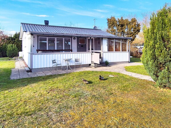 A single-story house with a covered porch, a small lawn, and a bird on the grass.