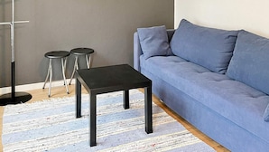 Een moderne woonkamer met een grijze bank, twee zwarte bijzettafels en een vloerlamp.