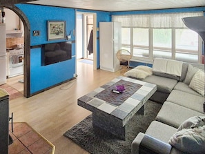 A living room with a sofa, a coffee table, and a television. There is a kitchen visible in the background. - 10 Person Holiday Home in Solvesborg (Sölvesborg)