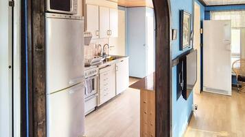 Una cocina con armarios blancos, microondas, refrigerador y lavamanos.