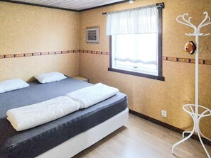 A single bed with white linens in a room with beige walls and a window with a white curtain.