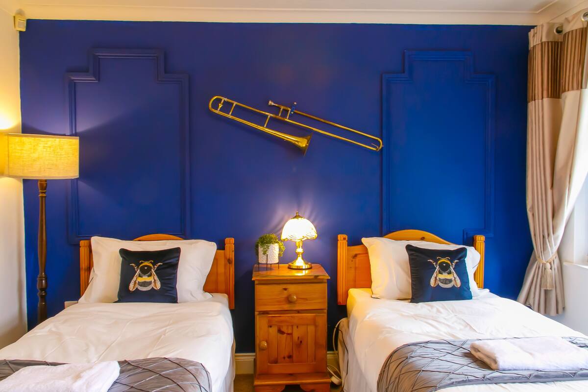 A room with two beds, a nightstand with a lamp, and a blue wall with a ladder.