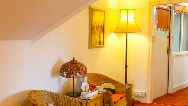 A cozy room with a wicker chair, a small table with a lamp, and a framed picture on the wall. - Mayfield Apartments (Sunderland)