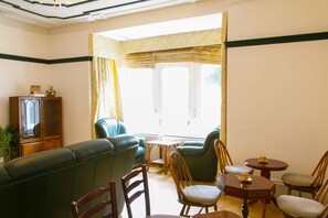 A living room with a green sofa, wooden chairs, a small round table, and a cabinet. - Mayfield Apartments (Sunderland)