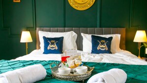 A neatly made bed with a green bedspread, two pillows with bee designs, a tray with cups and a towel, and two wall-mounted lamps. - Mayfield Apartments (Sunderland)