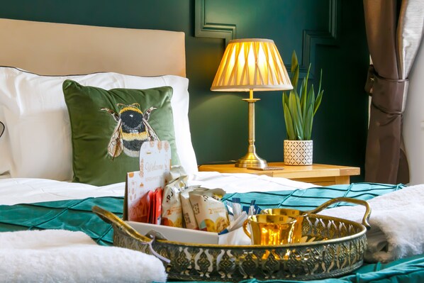 A neatly made bed with a green pillow, a bedside lamp, a tray with food items, and a potted plant.