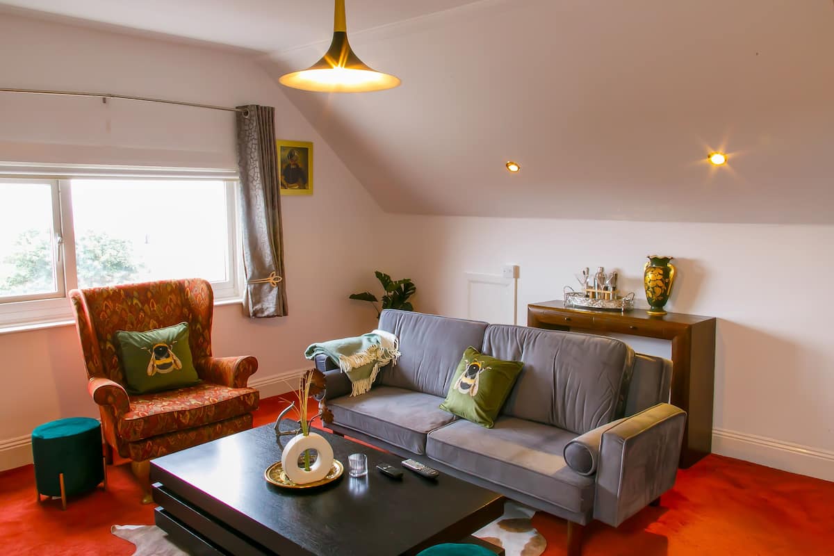 A living room with a sofa, armchair, and coffee table, a window with curtains, and a ceiling light.