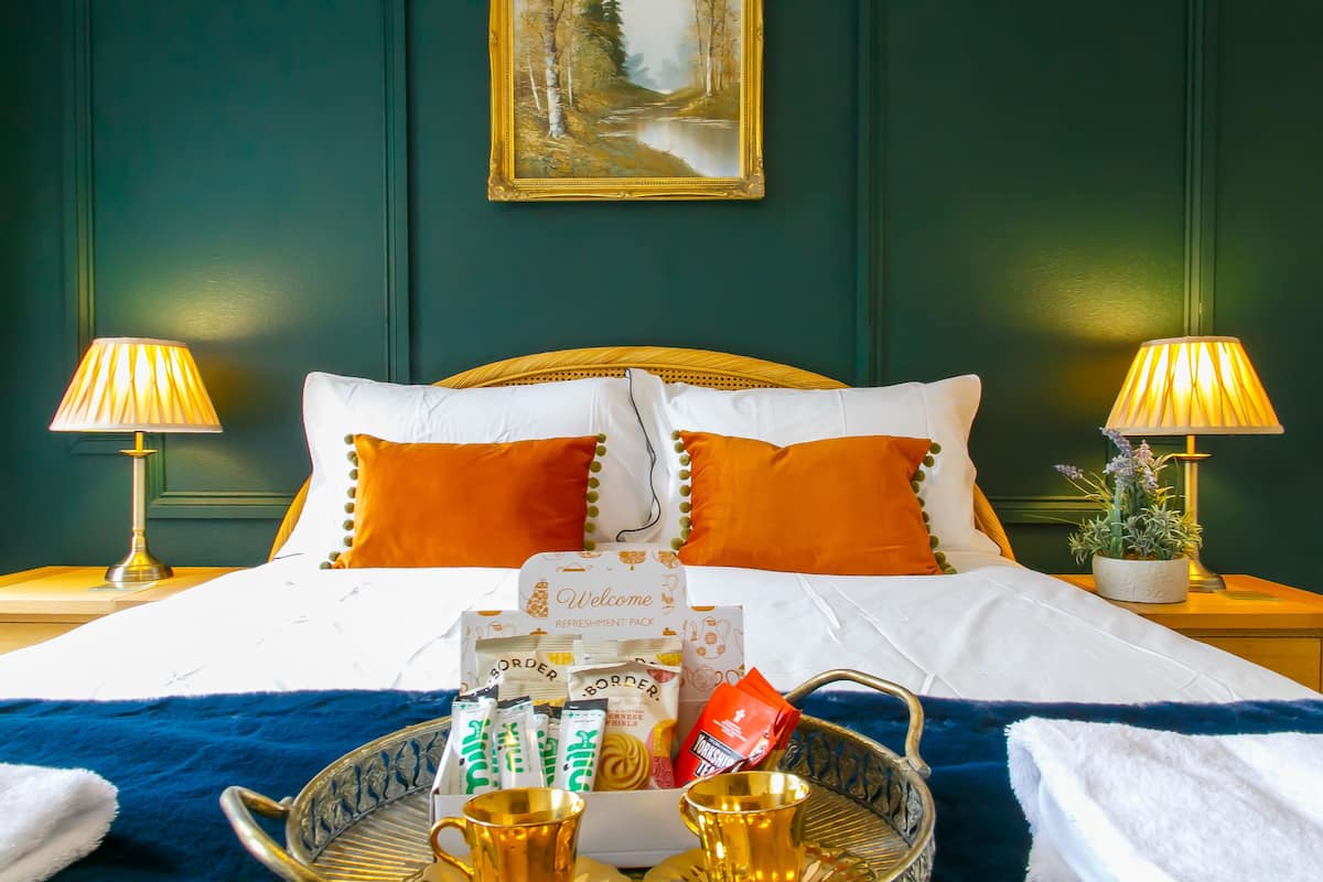 A neatly made bed with white and orange bedding, a tray with toiletries, and a painting on the wall.