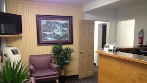 A reception area with a wooden reception desk, a purple armchair, a framed landscape painting, a potted plant, and a fire extinguisher. - Milestone Motel (Collingwood)