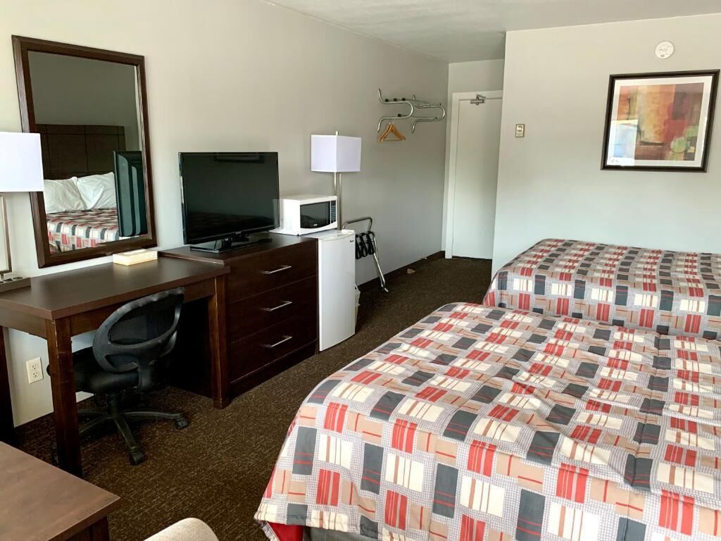 Habitació d'hotel amb un llit, una escriptori amb un ordinador, un televisor, un microones i un mirall.