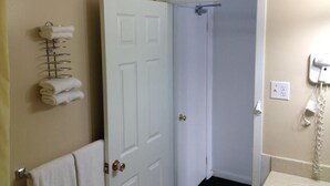 A bathroom with a white door, a towel rack with towels, a telephone, and a light switch on the wall. - Milestone Motel (Collingwood)