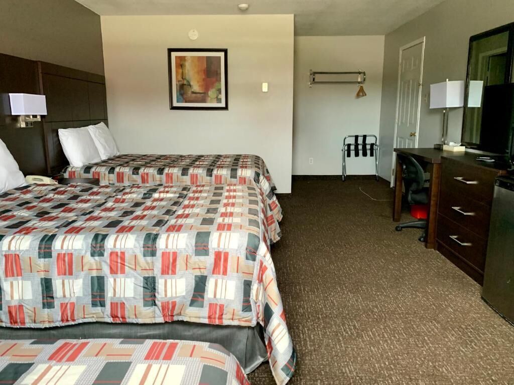 A hotel room with two beds, a desk, a chair, a television, and a painting on the wall.