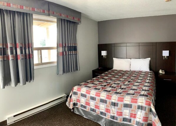 A hotel room with a bed, two bedside tables, a nightstand, a window with curtains, and a wall-mounted lamp. - Milestone Motel (Collingwood)
