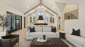 Ein geräumiges Wohnzimmer mit hoher Decke, einer Kandelaber und einer modernen Küche im Hintergrund.