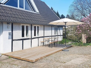 A house with a wooden deck, a covered patio with a table and chairs, and a garden with flowering plants. - 6 Person Holiday Home in Kettinge (Kettinge)