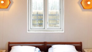A bedroom with two single beds, a window with a view of a fence and trees, and two wall-mounted lamps. - 6 Person Holiday Home in Kettinge (Kettinge)