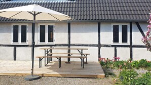 A house with a sloped roof, a wooden deck with a table and an umbrella, and a garden with flowers. - 6 Person Holiday Home in Kettinge (Kettinge)