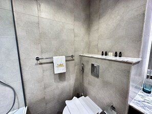 A modern shower area with a glass door, a towel rack with a towel, and a shelf with toiletries. - LuxBnB Paramount Midtown SeaView (Dubai)