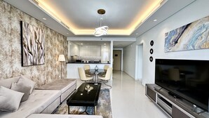 A modern living room with a sofa, a coffee table, a TV, and a kitchen in the background. - LuxBnB Paramount Midtown SeaView (Dubai)