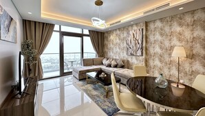 A modern living room with a sectional sofa, a dining table with chairs, a large window with curtains, and a city view. - LuxBnB Paramount Midtown SeaView (Dubai)
