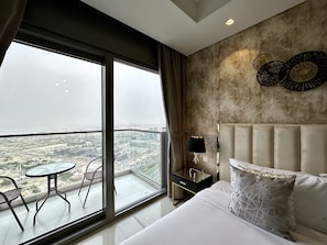 A hotel room with a large balcony, a bed with a headboard, a nightstand, and a table with chairs. - LuxBnB Paramount Midtown SeaView (Dubai)
