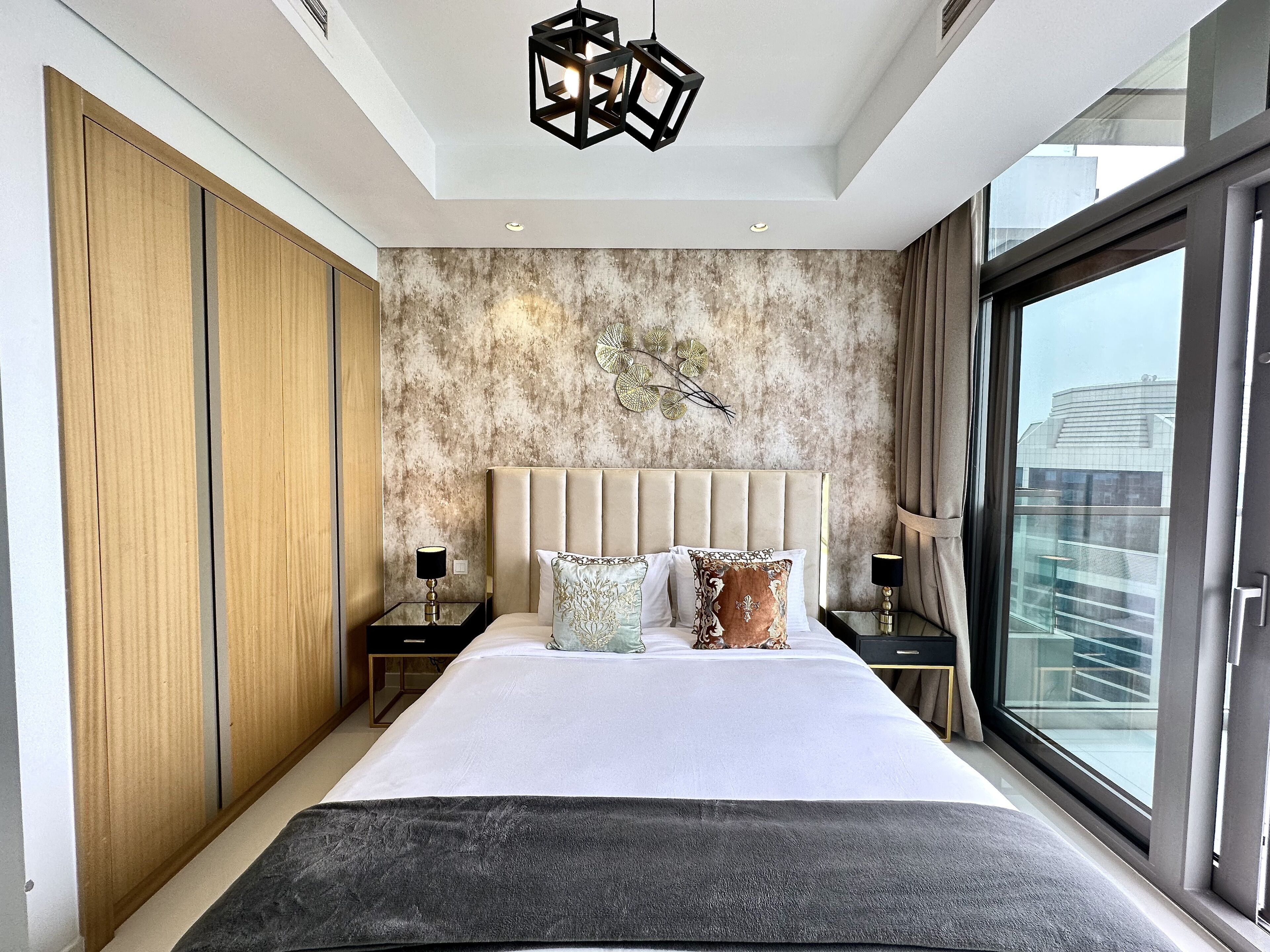 A modern bedroom with a large bed, wooden wardrobe, and a city view through a large window.
