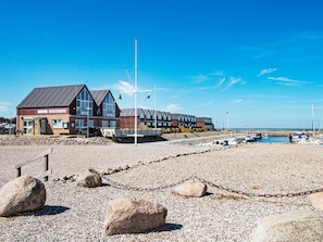 Experience the serene seaside setting at HAVNEKONTOR, where a pebbled beach and calm sea meet a modern coastal building.