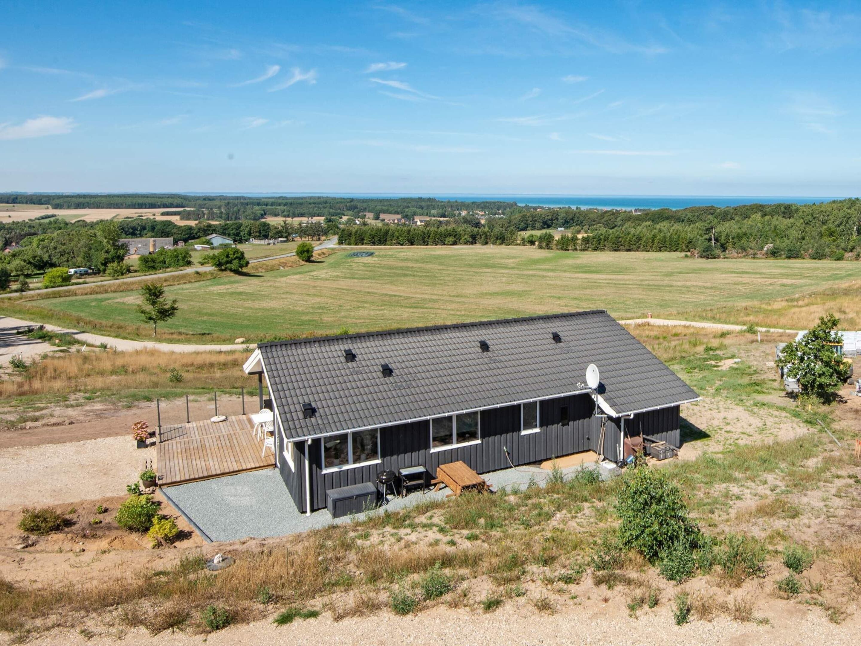A modern house with a large deck, a covered outdoor area, and a view of the surrounding countryside.