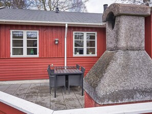 En rød bygning med en stensokkel, et bord med stole og en potteplante.