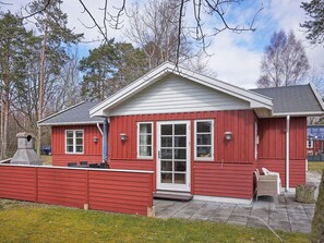 A red wooden cabin with a white door, large windows, and a chimney.