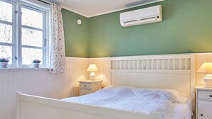 A bedroom with a bed, bedside tables, an air conditioner, a window with curtains, and a view of trees outside. - 4 Person Holiday Home in Ronne-by Traum (Ronne)