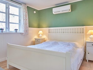 A bedroom with a bed, bedside tables, an air conditioner, a window with curtains, and a view of trees outside. - 4 Star Holiday Home in Ronne (Ronne)