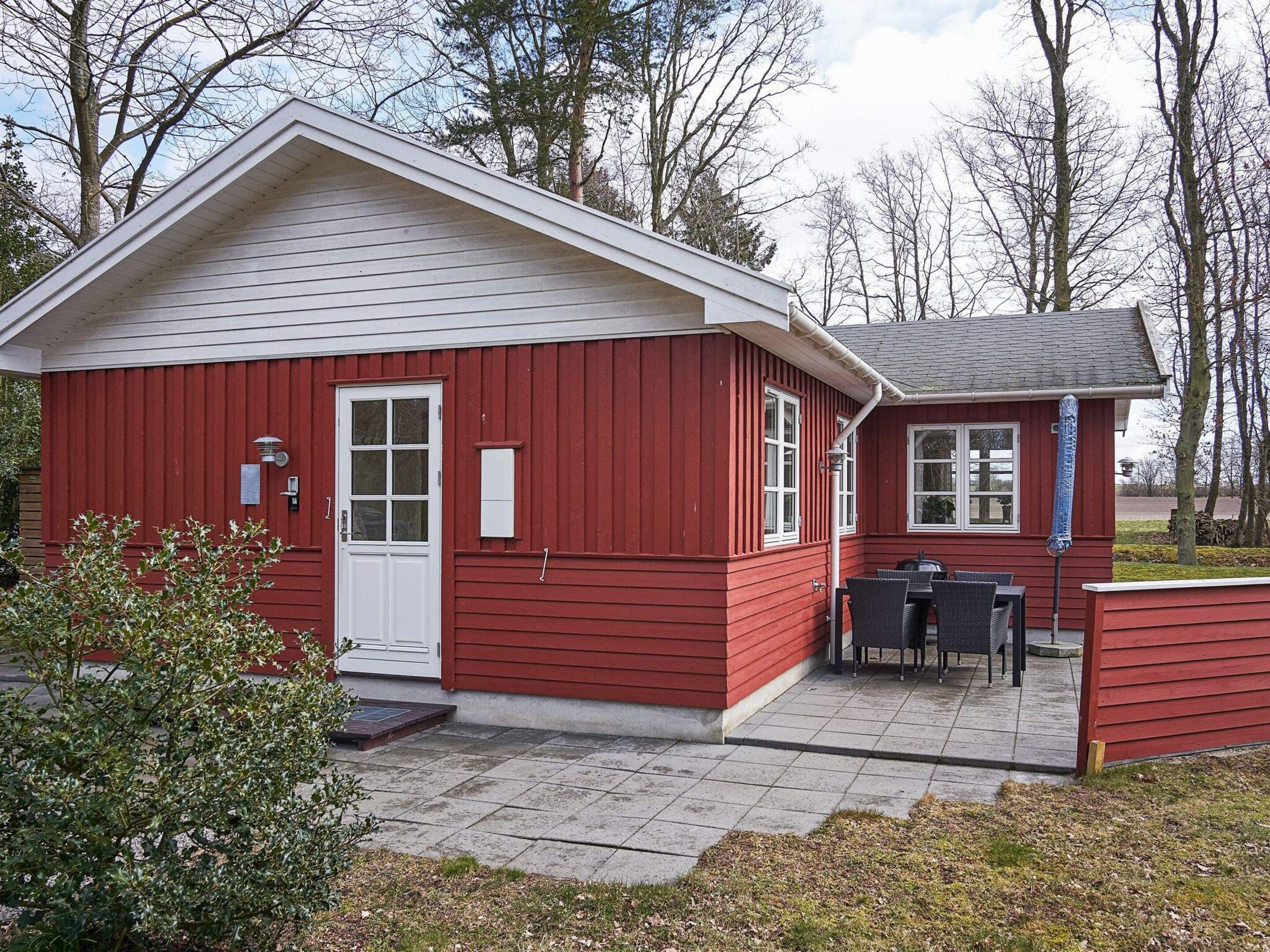 A red building with a white door, a small outdoor seating area, and a clear sky.