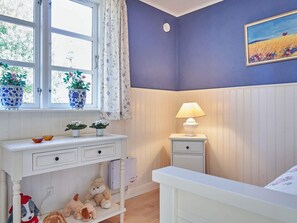 A room with a white dresser, a nightstand with a lamp, and a window with curtains.