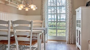 A dining area with a table and chairs, a window with curtains, and a cabinet. - 4 Person Holiday Home in Ronne-by Traum (Ronne)