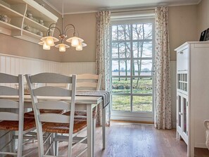 A dining area with a table and chairs, a window with curtains, and a cabinet. - 4 Star Holiday Home in Ronne (Ronne)