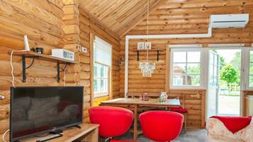 Interior acolhedor de uma cabana, com decoração em madeira, televisão, mesa de jantar com cadeiras e uma janela.