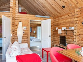 Interior de una cabaña de troncos con una cama, un sofá, una mesa y un televisor.
