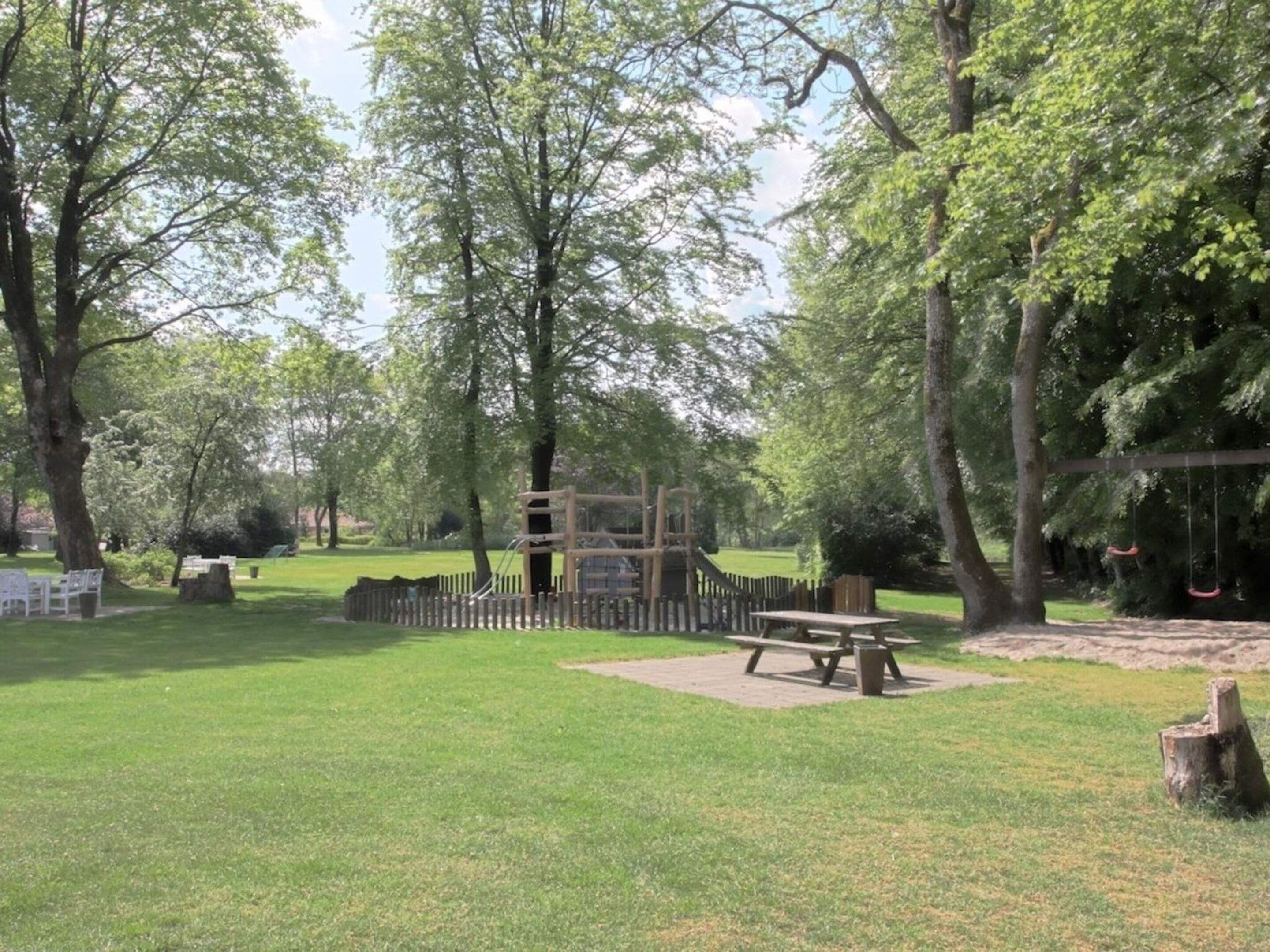 A park with a picnic table, playground equipment, and a swing set.