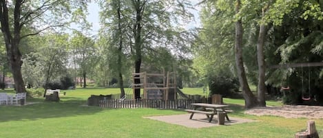 A park with a picnic table, playground equipment, and a swing set.