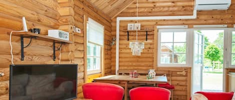 A cabin interior with a wooden interior, a television, a dining table with chairs, and a window.