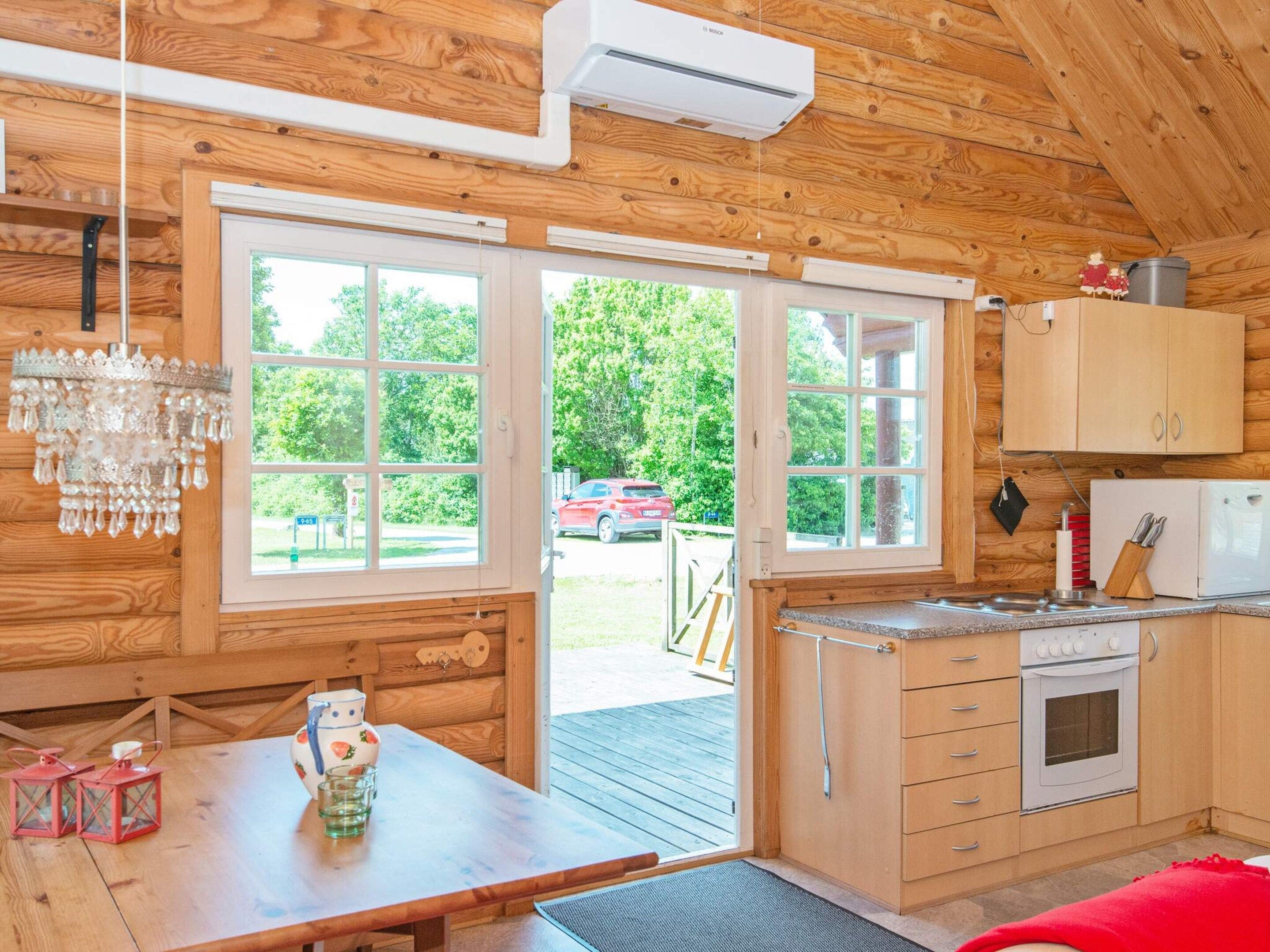 A wooden cabin interior with a kitchen, dining area, and large windows.