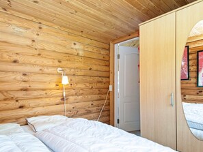 A wooden-paneled room with a bed, a bedside lamp, and a wardrobe.