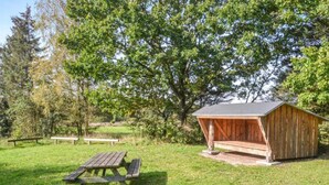A rustic wooden shed with a sloped roof, a picnic table, and benches in a grassy area with trees in the background. - 5 Person Holiday Home in Hovborg (Hovborg)