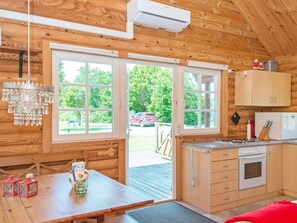 A wooden cabin interior with a kitchen, dining area, and large windows.