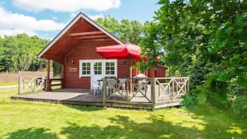 A wooden cabin with a deck, a table with chairs, and a red umbrella.