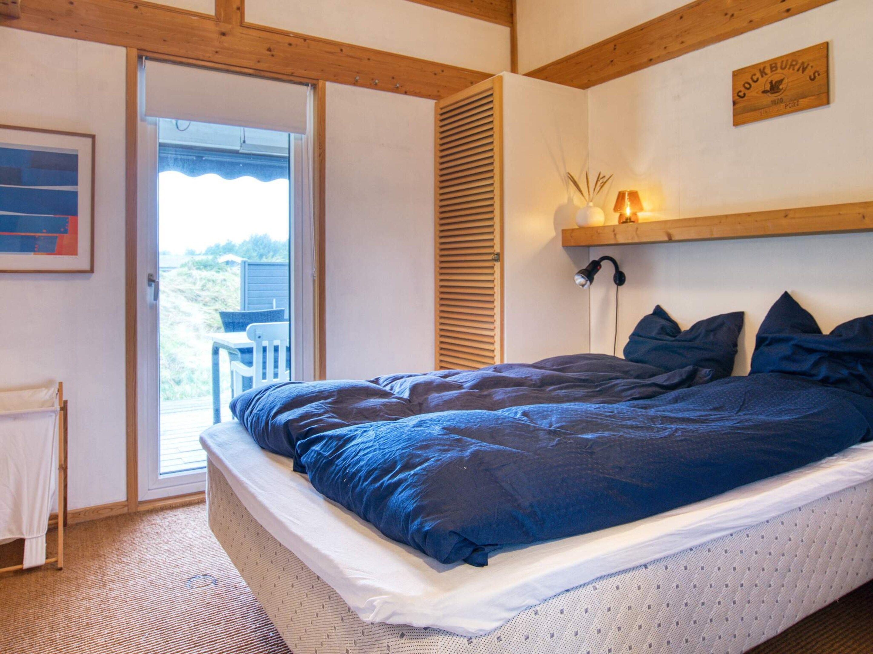 Une chambre à coucher avec un lit, une fenêtre, une porte et une étagère fixée au mur.