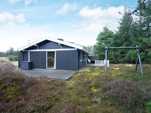 A modern house with a large deck, a swing set, and a white fence.