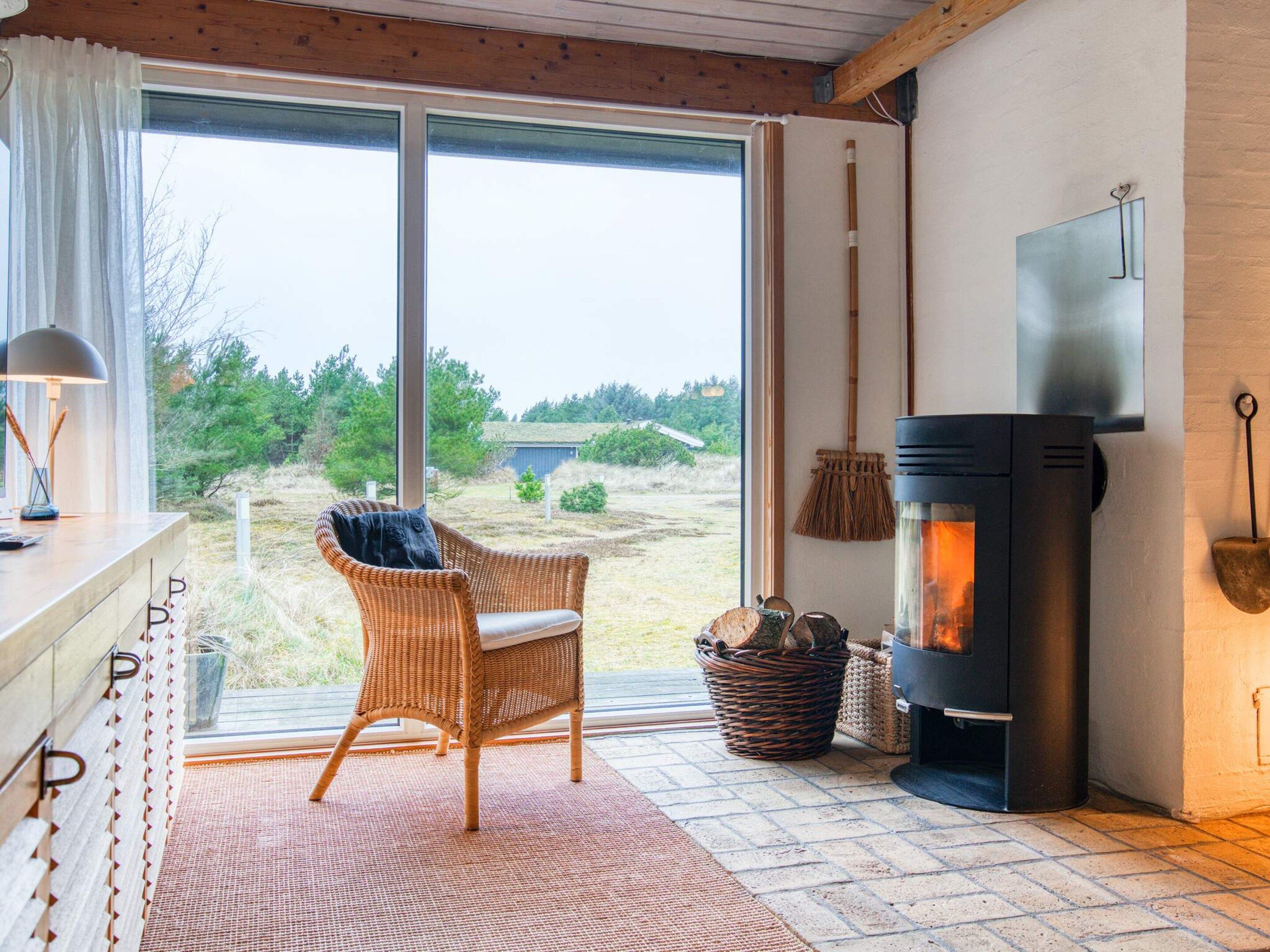A cozy room with a large window, a wicker chair, a fireplace, and a TV.
