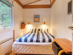 A bedroom with a bed, a bedside table, a window, and a wall-mounted light fixture.